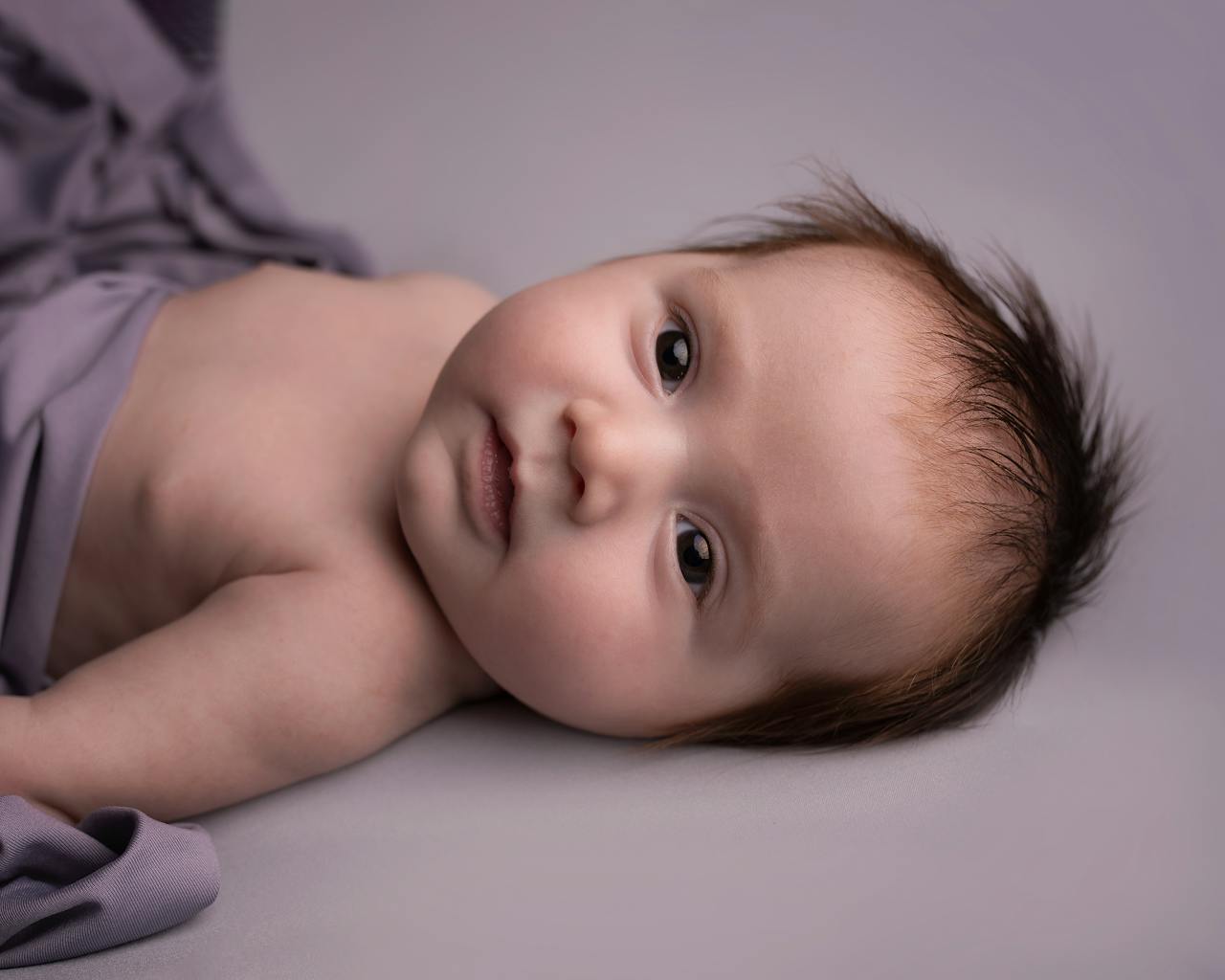 Close-up of an adorable newborn baby lying comfortably on a soft purple blanket.